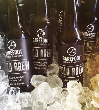 Barefoot Cold Brew bottles with black labels on a wooden surface surrounded by ice