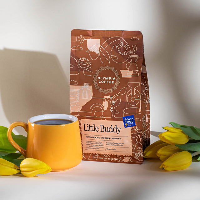 Little Buddy coffee bag with a bright yellow mug and yellow tulips on a white countertop.