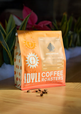 Arborvitae coffee bag in bright orange packaging with a tree logo and dark blend label on a wooden surface