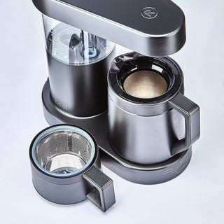 Able reusable coffee filter with perforated metal basket and blue rim shown beside a drip coffee maker.