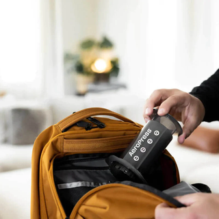 AeroPress being tucked into a mustard backpack to highlight its portable travel use
