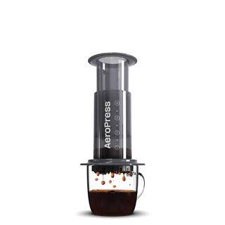 AeroPress coffee maker with transparent chamber and plunger over a glass carafe of coffee.