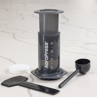 AeroPress coffee maker on a marble counter with its base and cleaning accessories nearby for setup