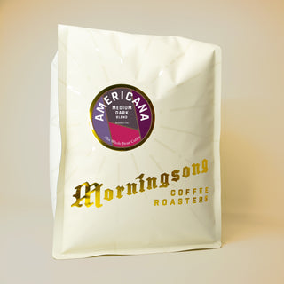 Americana Classic Roast coffee bag with circular purple label stating Medium Dark Blend and sunrise motif