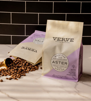 Aster coffee bag by Verve on a white marble counter with a brass scoop and scattered coffee beans.
