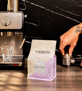 Espresso machine with a Verve Aster coffee bag in the foreground on a dark marble counter.