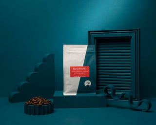 Bravissimo whole bean coffee bag on teal background with scattered coffee beans in the foreground.