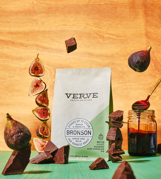 Bronson coffee bag from Verve surrounded by dark chocolate pieces and fig slices on a warm wooden surface