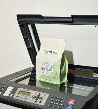 Bronson coffee bag on a marble counter with coffee beans spilled and a copier in the background