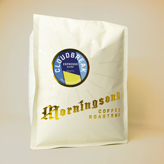 White coffee bag featuring a round blue and gold Cloudbreak Espresso Blend label with radial lines.