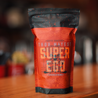 Close-up of Super Ego coffee bag with a dark speckled top and bold orange red body featuring Thou Mayest branding