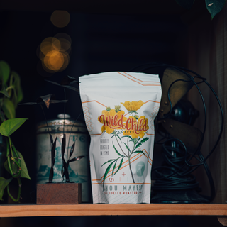 Wild Child coffee bag with bright yellow flower illustration on a shelf with soft bokeh lights.