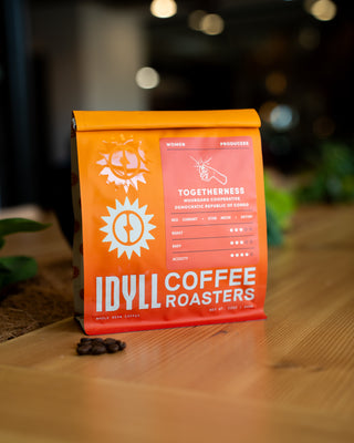 Bright orange coffee bag with sun logo and Togetherness label from Muungano Cooperative DR Congo on a wooden surface.