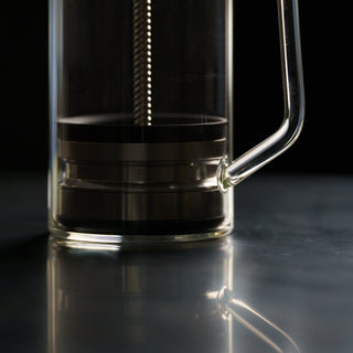 Close up of The BIRD glass brewing chamber with metal fittings against a dark background