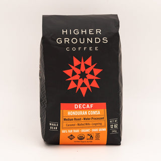 Higher Grounds Decaf Honduras bag with black packaging and an orange label reading Decaf Honduras Comsa beside a blue mug.