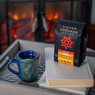 Higher Grounds Decaf Honduras bag on a table with a blue mug and stacked books in the background.