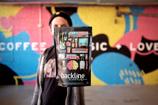 Person holding Backline Blend bag up in front of a vibrant graffiti mural