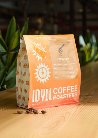 Foreglow espresso blend coffee bag with an illustrated label on orange packaging resting on a wooden surface