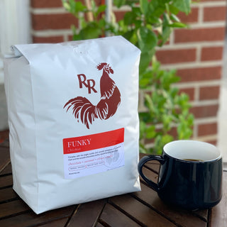White Funky Chicken coffee bag with red rooster logo on a wooden table beside a black mug.