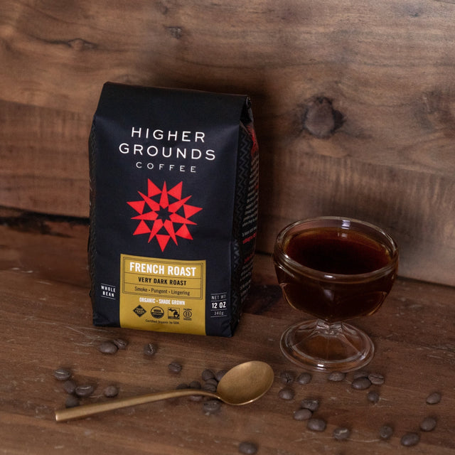 French Roast coffee bag on a wooden table with scattered coffee beans and a small glass jar nearby.