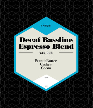 Decaf Bassline Espresso Blend coffee packaging with a cream label and blue framed badge against a black geometric background
