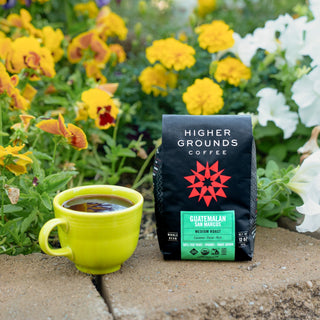 Guatemalan San Marcos medium roast bag from Higher Grounds with a green label and orange roast panel beside a yellow coffee mug
