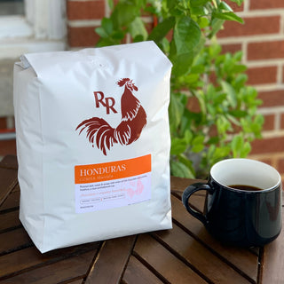 Close up of Honduras COMSA Marcala coffee bag with Red Rooster logo and orange label beside a mug