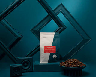 Il Primo espresso packaging with coffee beans spilled on a blue teal surface