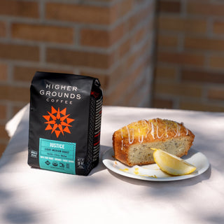 Justice coffee bag by Higher Grounds on a table with a pastry and a brick wall backdrop.