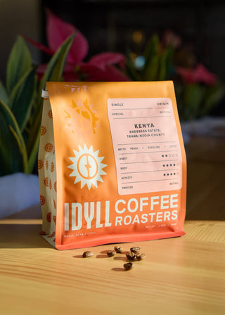 Orange Kenya coffee bag with Endebess Estate label on a wooden surface and white peach notes.