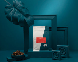 L Alba coffee bags displayed on a teal shelf with a large leaf prop in the foreground