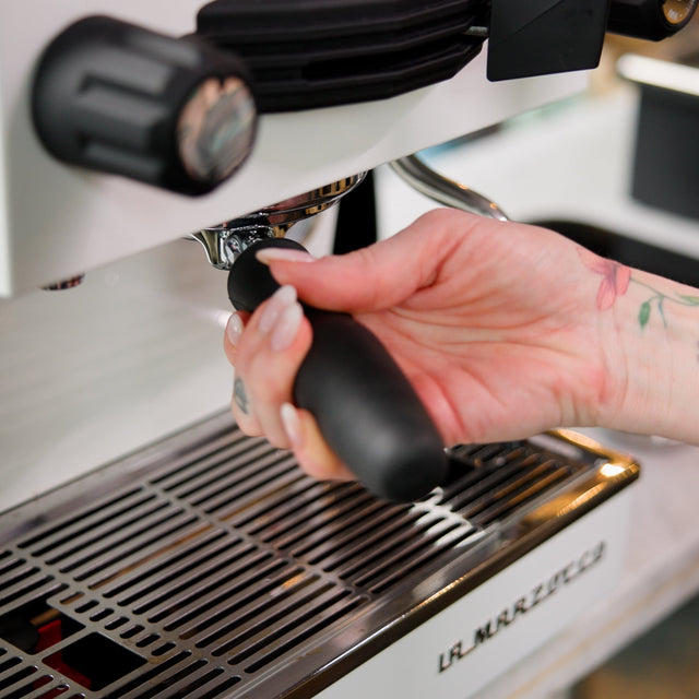 Close-up of hand tamping espresso into a portafilter on a shiny espresso machine