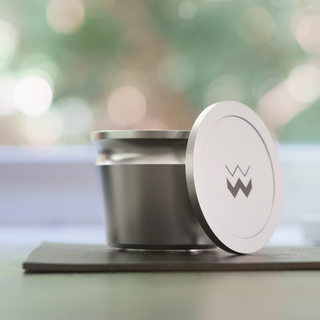 The Key compact stainless steel coffee grinder with circular lid leaning against the body and a logo on the lid.