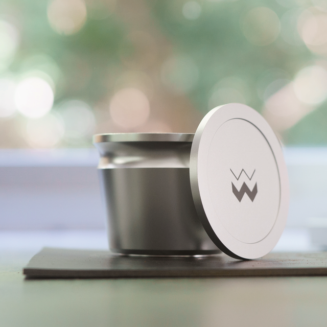 The Key compact stainless steel coffee grinder with circular lid leaning against the body and a logo on the lid.