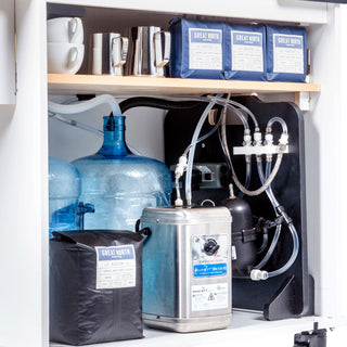 Inside the cart cabinet with blue water jugs, coffee bags, and hoses and controls for the espresso system