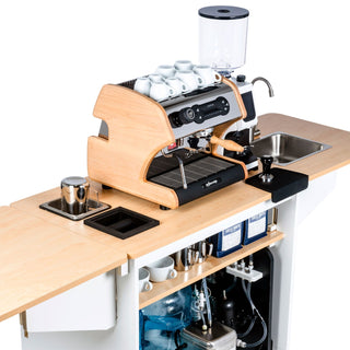 Close up of LUCCA espresso machine on a mobile cart with wooden wrap cups on top and sink visible at the edge