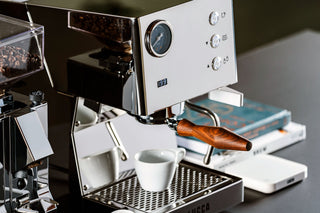 Wood bottomless portafilter with wooden handle mounted on espresso machine.