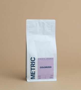 Colorized coffee bag with lavender label on a white standup pouch against a tan backdrop