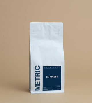 White coffee bag with a dark blue EN MASSE label on the front against a tan backdrop.