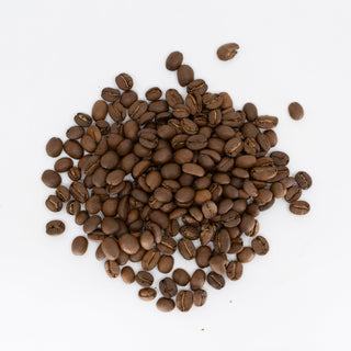 Roasted El Manzano coffee beans spread across a white surface.