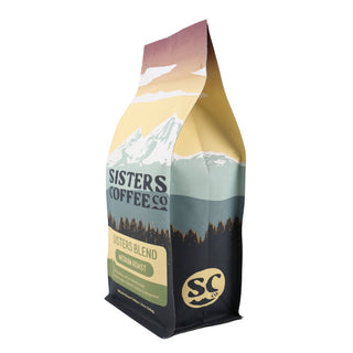 Angled side view of Sisters Blend coffee bag featuring mountain artwork and green medium roast badge