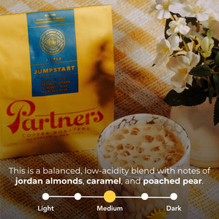 Jumpstart yellow coffee bag with blue label next to a blue crate and a hand holding a red Partners bag