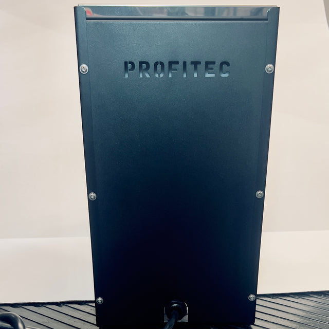 Back view of a dark blue Profitec GO espresso machine in an open box with embossed PROFITEC letters and visible screws.