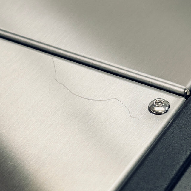 Close up of brushed stainless steel surface with a diagonal seam and corner screw.