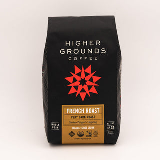 French Roast coffee bag from Higher Grounds on a wooden table with blueberries and a spoon beside.