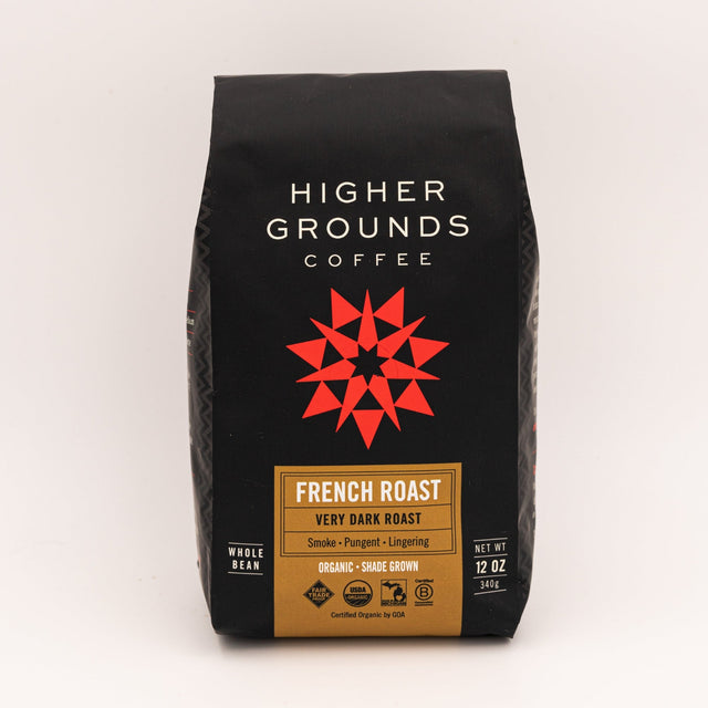 French Roast coffee bag from Higher Grounds on a wooden table with blueberries and a spoon beside.
