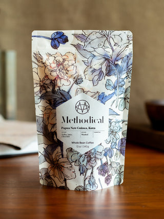 Floral patterned coffee bag with a white label reading Methodical Papua New Guinea Kuta Whole Bean Coffee