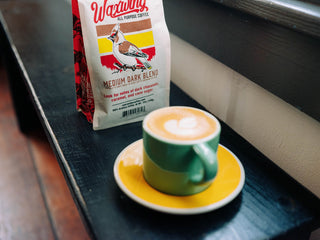 Waxwing Medium Dark Blend bag with bird artwork and a cup of coffee on a saucer