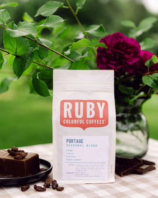 Portage Seasonal Blend coffee bag displayed outdoors among green leaves and a purple flower