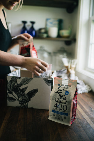Person packs Red Rooster 4&20 French Roast coffee bags in a kitchen